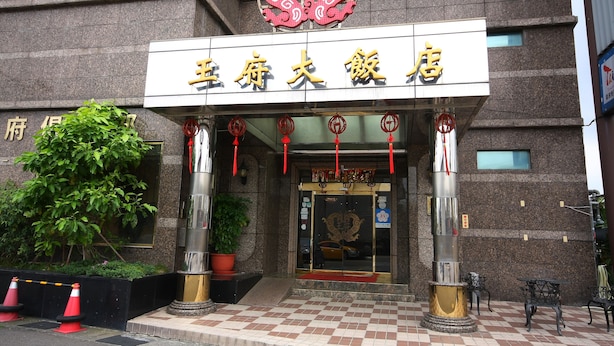 Een hotelingang met een traditioneel Chinees architectuurontwerp, met een rood draken embleem boven de ingang en een ruitpatroon vloer dat naar de deuren leidt.