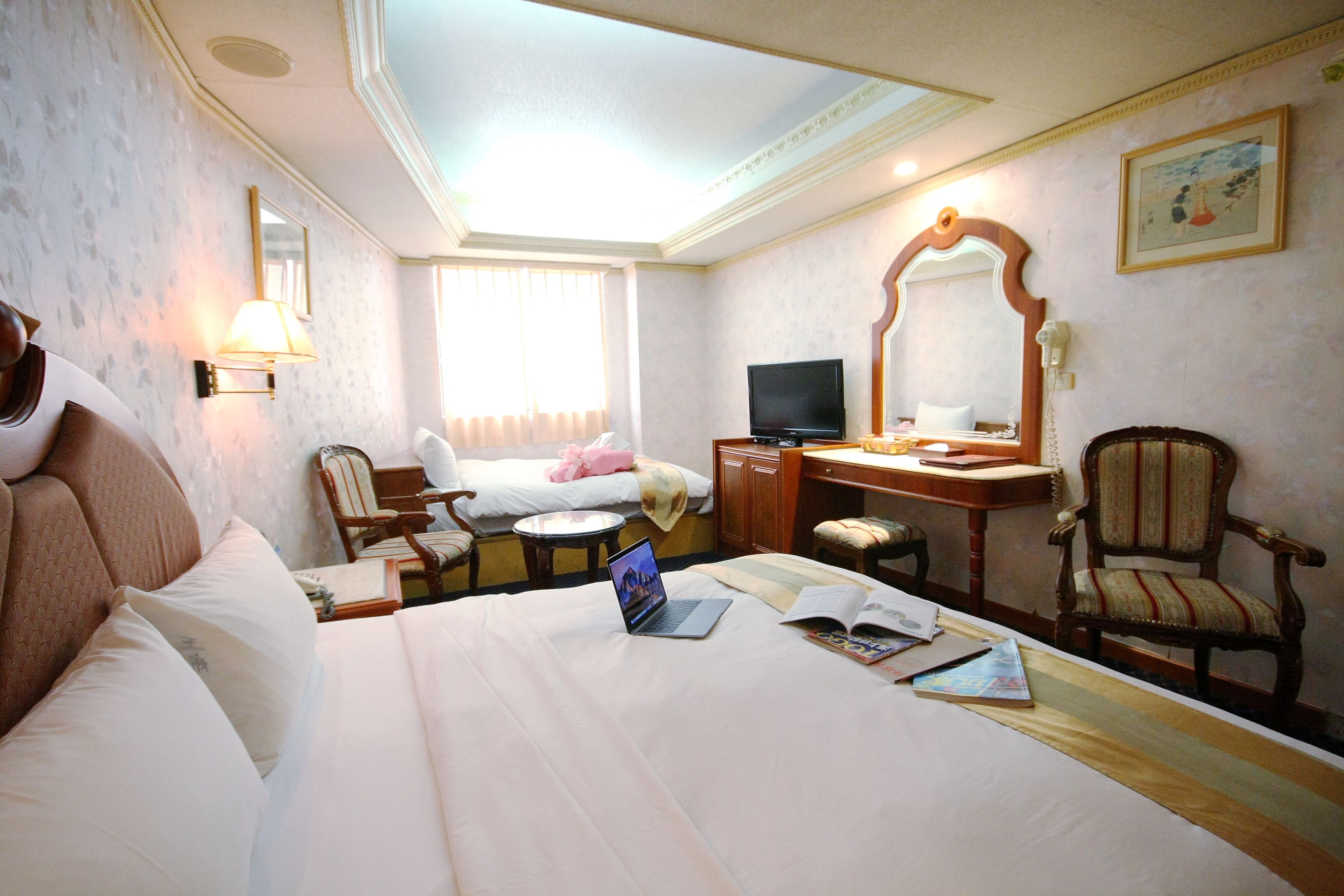 A hotel room with a bed, a desk with a laptop, a chair, a television, and a large mirror.