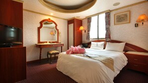 Een hotelkamer met een groot bed, een televisie, een bureau met stoel, een spiegel en een raam met gordijnen.