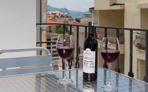 Una mesa con una botella de vino y dos copas en un balcón con vistas a la ciudad.