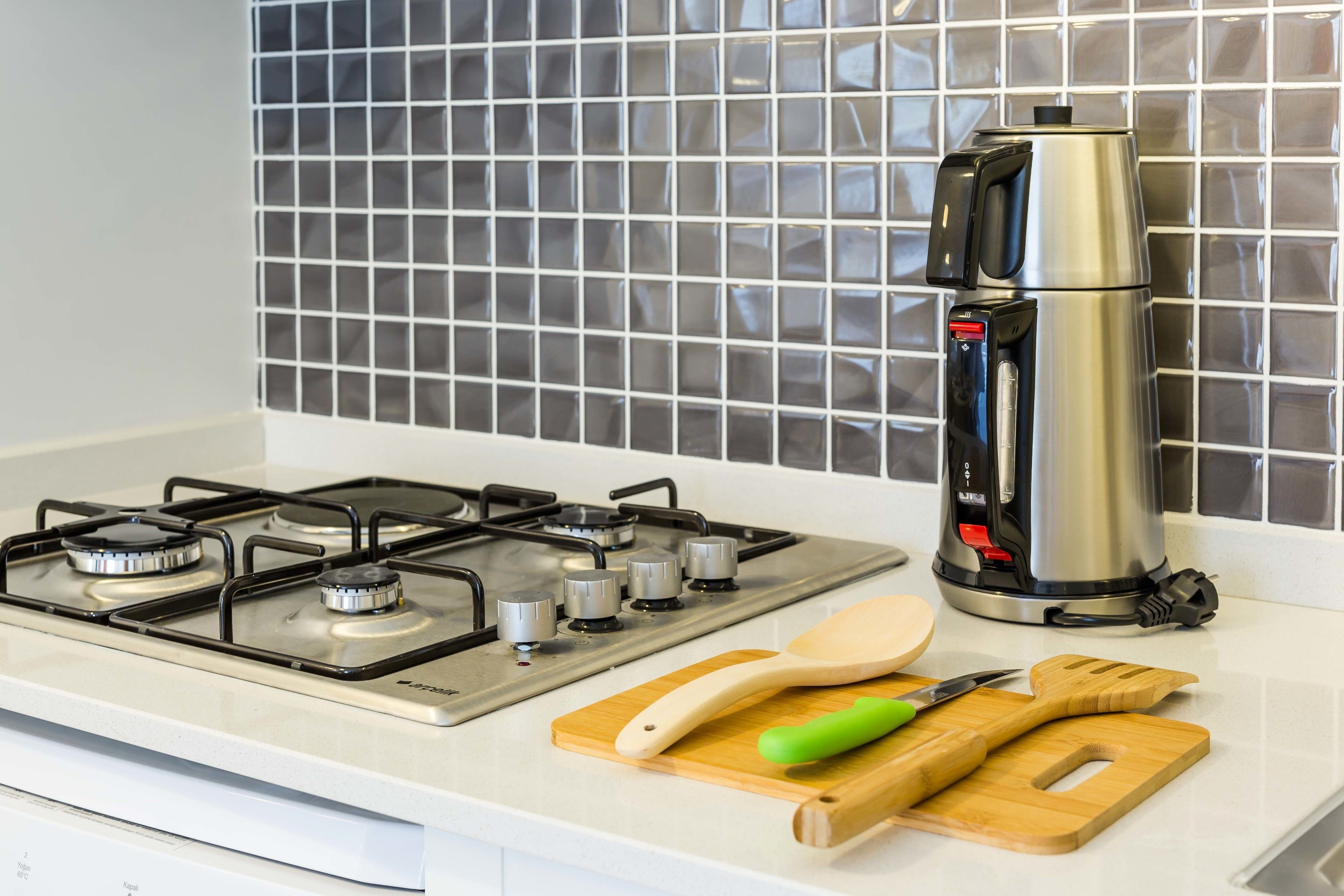 Una cocina con estufa a gas, cafetera, tabla de cortar de madera y un cuchillo.