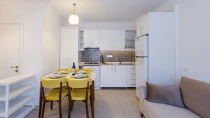 Cocina compacta con armarios blancos, una mesa de comedor para cuatro personas y un sofá beige en la sala de estar.