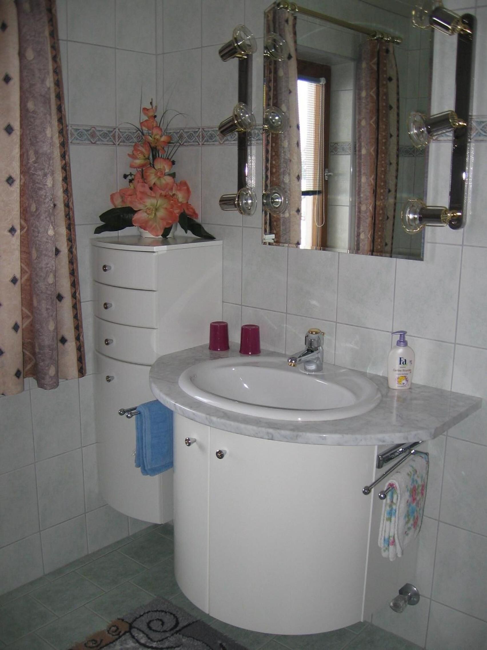 Un baño con un lavamanos blanco, un espejo y un perchero para toallas.