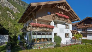 A traditional chalet with a balcony adorned with flowers, a garden with colorful flowers, and a mountainous backdrop. - Gästehaus Renate (Laengenfeld)