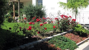 A garden with red roses and various plants in front of a building with a balcony. - Gästehaus Renate (Laengenfeld)