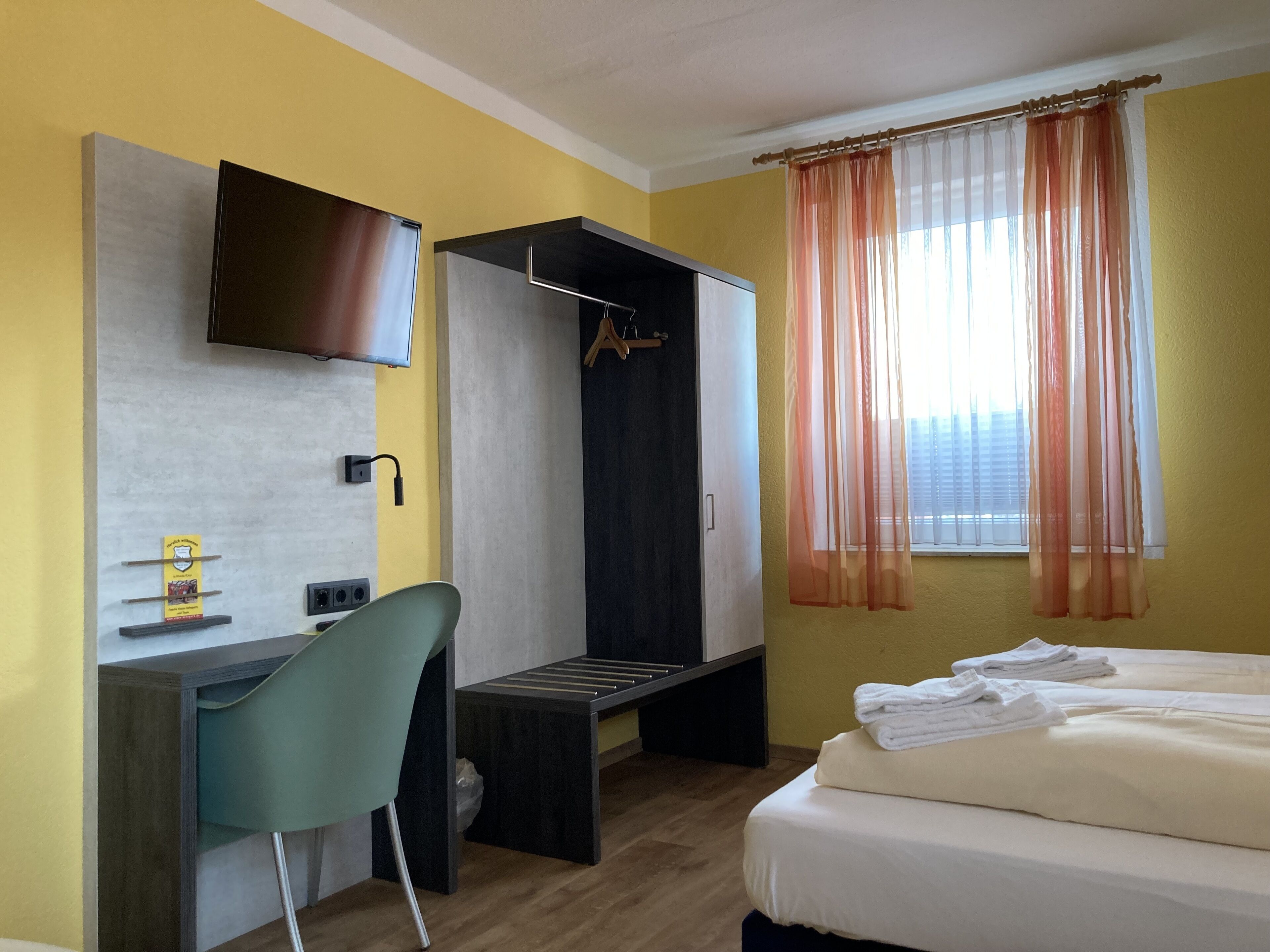 Une chambre d’hôtel comprenant un lit, un bureau, une chaise, un téléviseur fixé au mur et une fenêtre avec des rideaux.