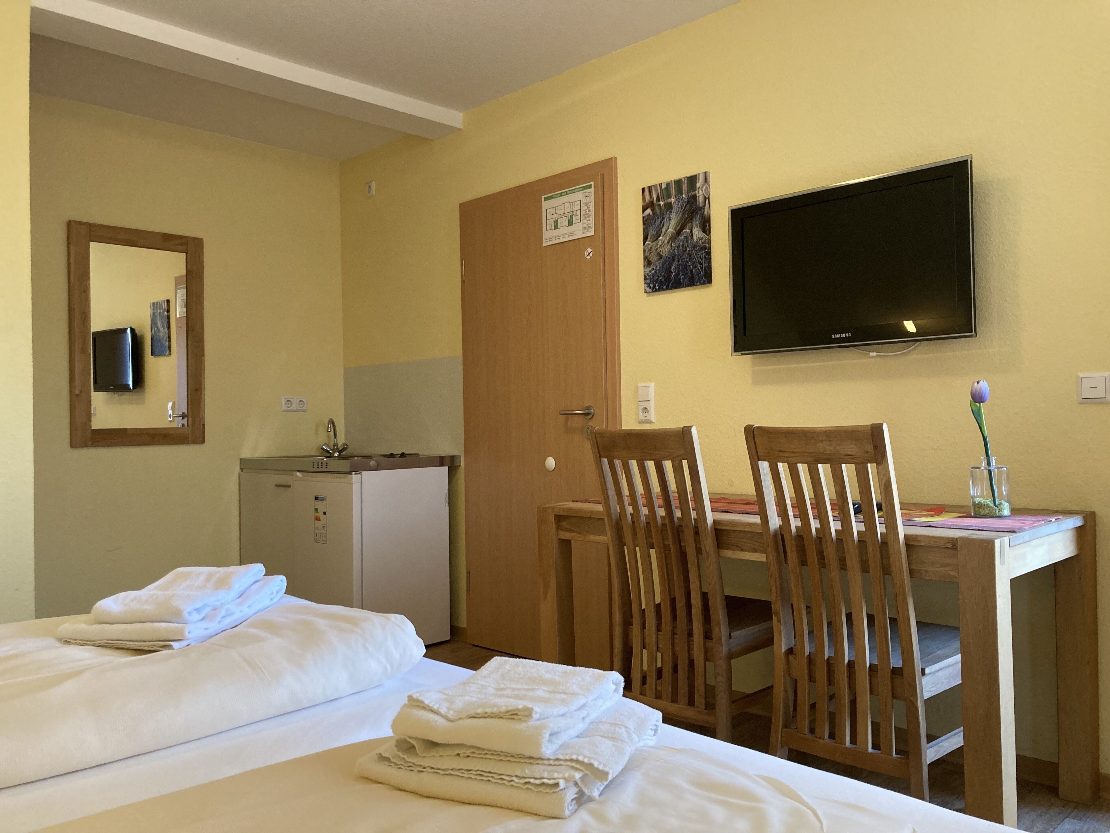 A hotel room with two beds, a desk with a chair, a television, and a door with a sign.