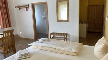 Habitación de hotel con cama, una silla de madera, una mesita, un espejo y baño visible a través de una puerta abierta.