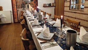A long dining table set for a meal with chairs, candles, and a view of a brick wall and a door. - Landhotel Vosse-Schepers (Rhede)