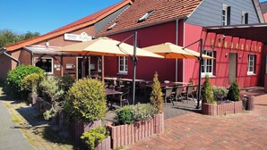 A restaurant with outdoor seating, a red building, and a sign indicating a reception area. - Landhotel Vosse-Schepers (Rhede)