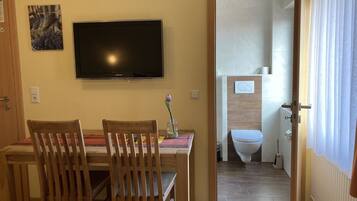 A room with a dining table, two chairs, a flat-screen TV, and a bathroom visible through an open door.