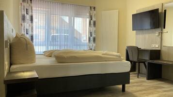 A hotel room with a bed, a desk, a chair, a TV, and a window with curtains.