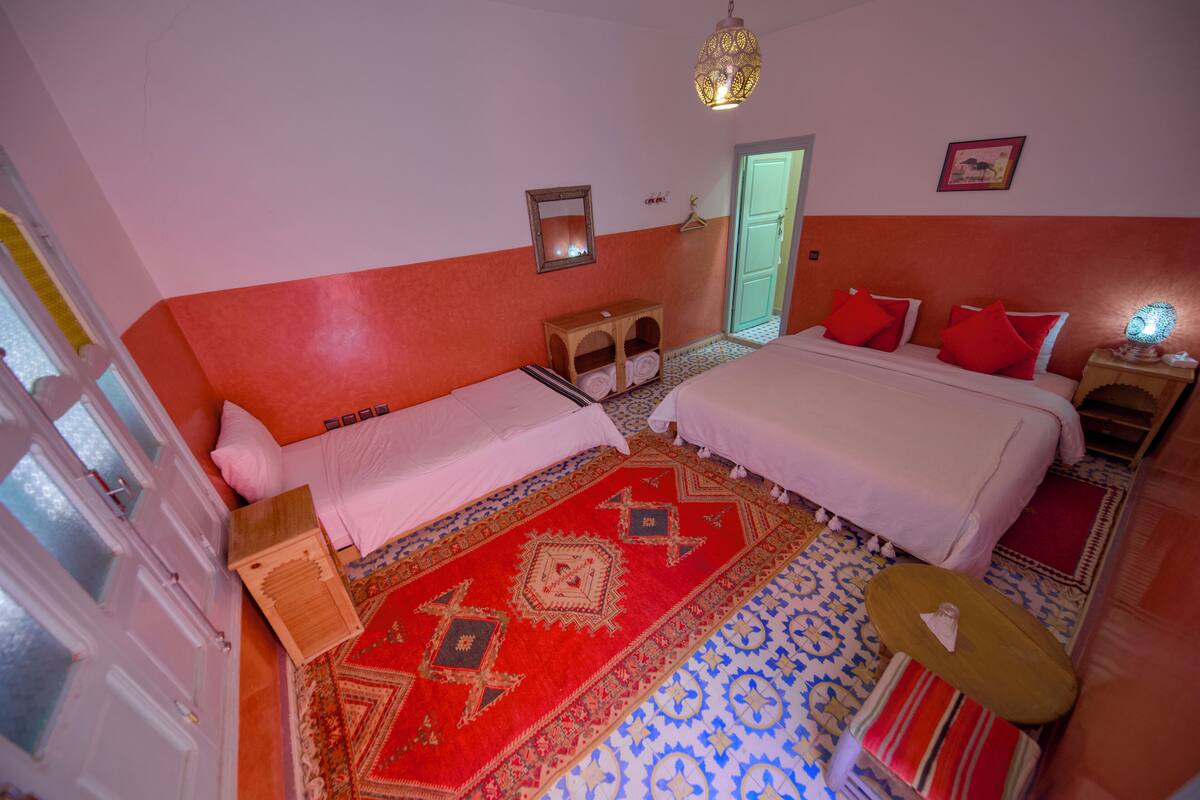 A room with two beds, a patterned rug, a hanging light fixture, and a door.