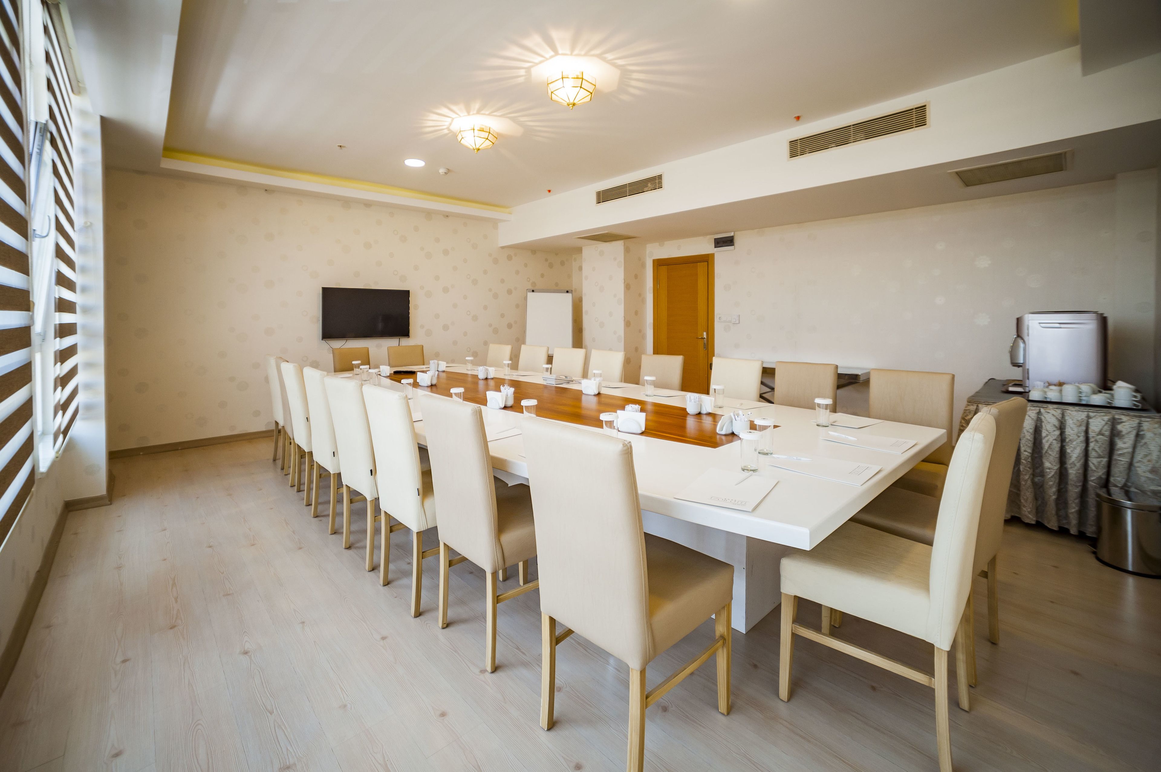A conference room with a long table, chairs, a flat-screen TV, and a coffee machine.