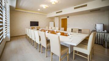 A conference room with a long table, chairs, a flat-screen TV, and a coffee machine.