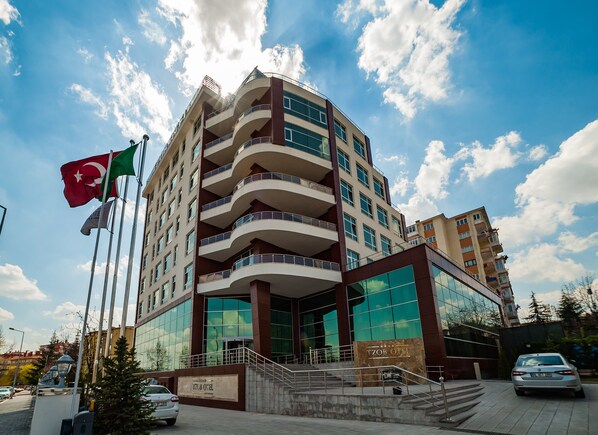 Un hotel de varios pisos con un diseño moderno, que cuenta con balcones, ventanas amplias y una entrada destacada con una escalera.