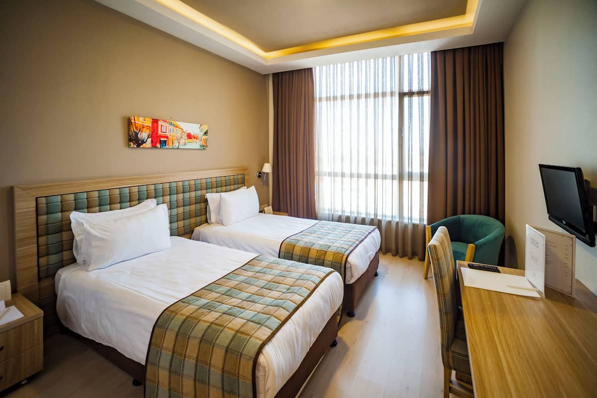 A hotel room with two beds, a desk, a chair, a TV, and a window with curtains.