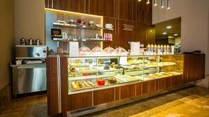Una vitrina de pastelería con diversos pasteles y productos horneados, una máquina de café y un refrigerador con productos.