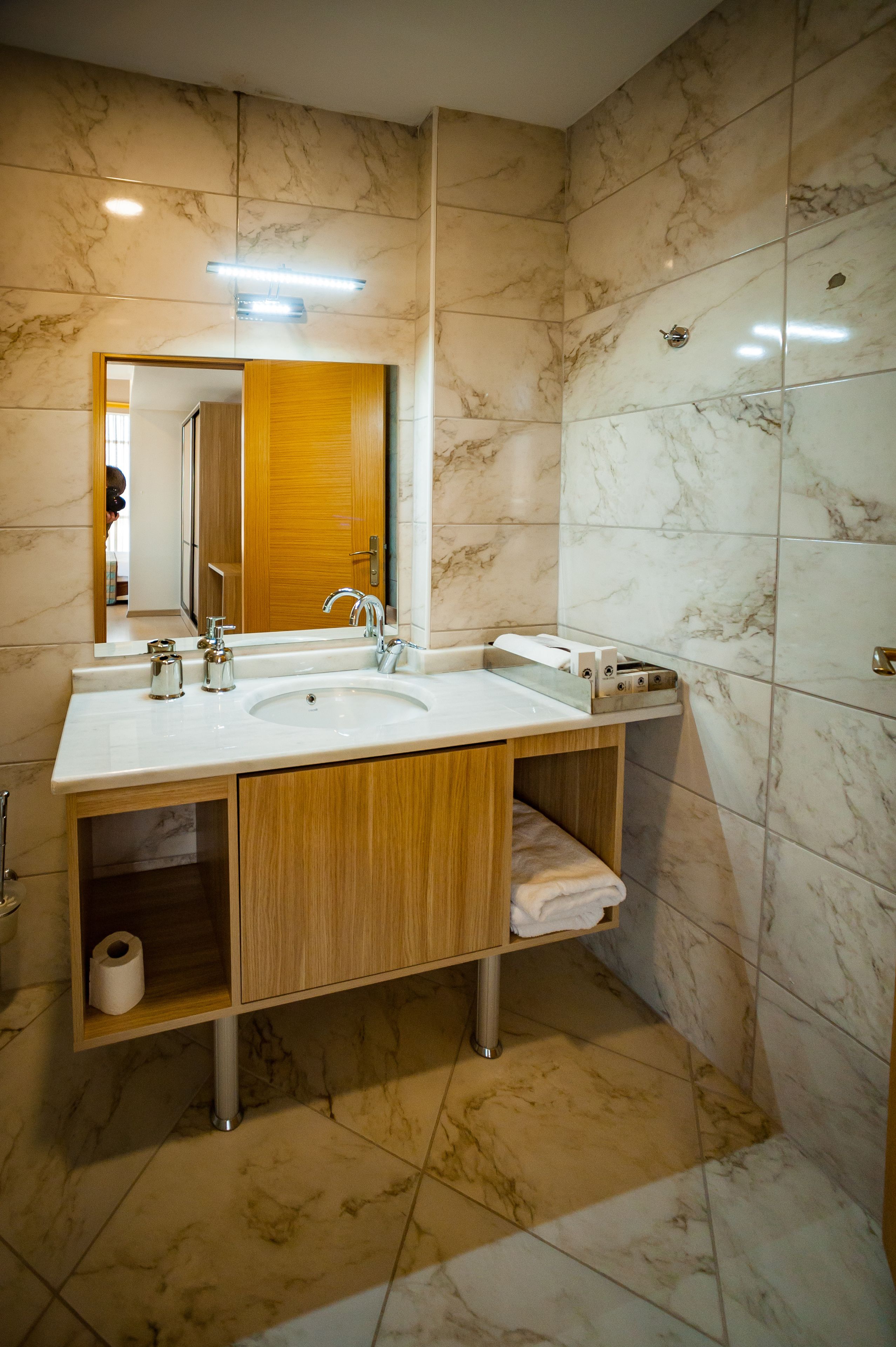 Une salle de bain avec un mur recouvert de carreaux de marbre, un meuble-lavabo en bois, un miroir et un porte-serviettes.
