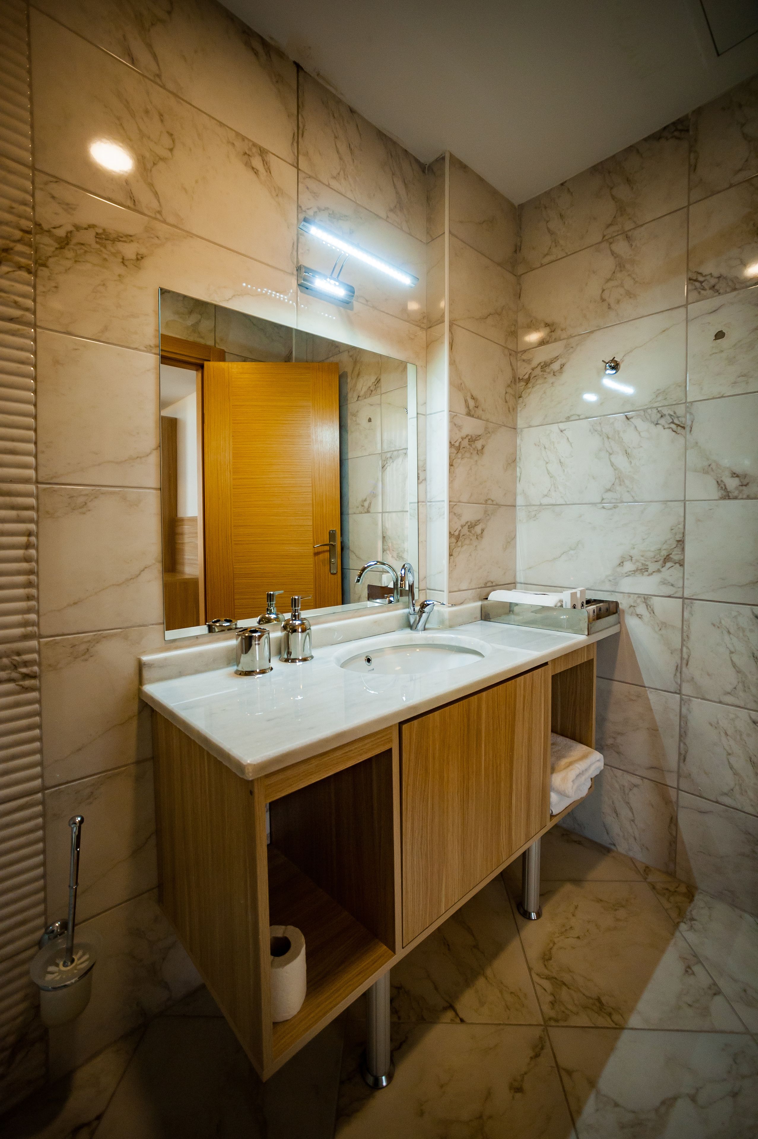 A modern bathroom with a double sink vanity, marble tiles, a wooden cabinet, and a mirror.