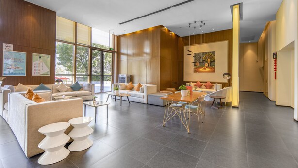 A spacious hotel lobby with a modern design, featuring a large seating area with sofas and a dining table, large windows providing natural light, and a wooden accent wall. - MiniMax Hotel Shanghai Songjiang (Shanghai)