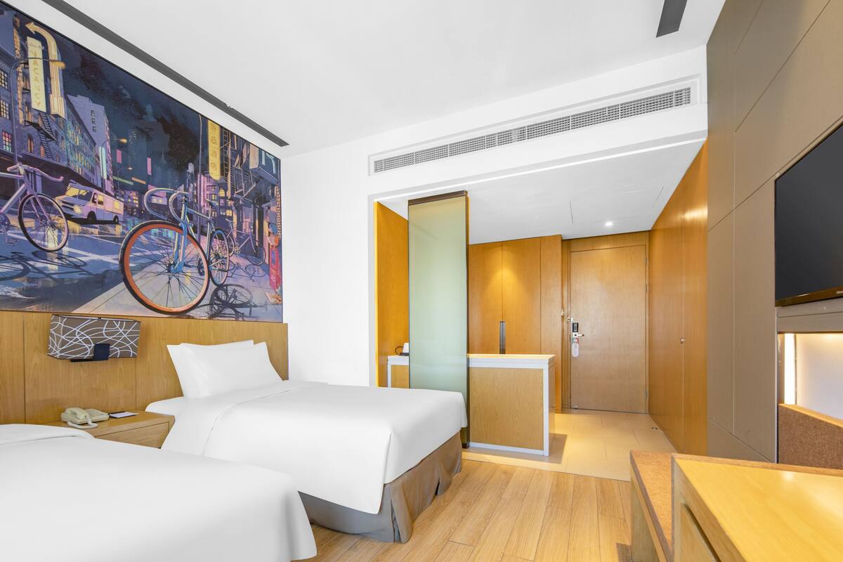 Ein Hotelzimmer mit zwei Betten, einem großen Gemälde eines Fahrrads an der Wand, einem Holzschrank und einem Fernseher auf der rechten Seite.