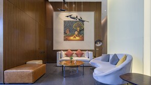 A modern interior with a sofa, armchair, and ottoman in a well-lit room with wooden paneling and a large artwork on the wall. - MiniMax Hotel Shanghai Songjiang (Shanghai)