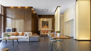 A modern hotel lobby with a sofa, dining table, and chairs, wooden paneling, and a large painting on the wall. - MiniMax Hotel Shanghai Songjiang (Shanghai)