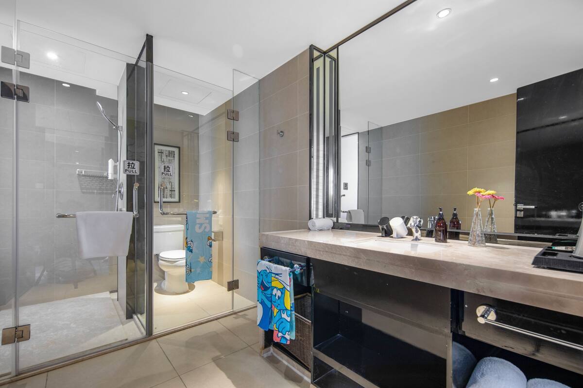 Ein modernes Badezimmer mit Duschkabine aus Glas, Toilette und Waschbecken mit Spiegel darüber.