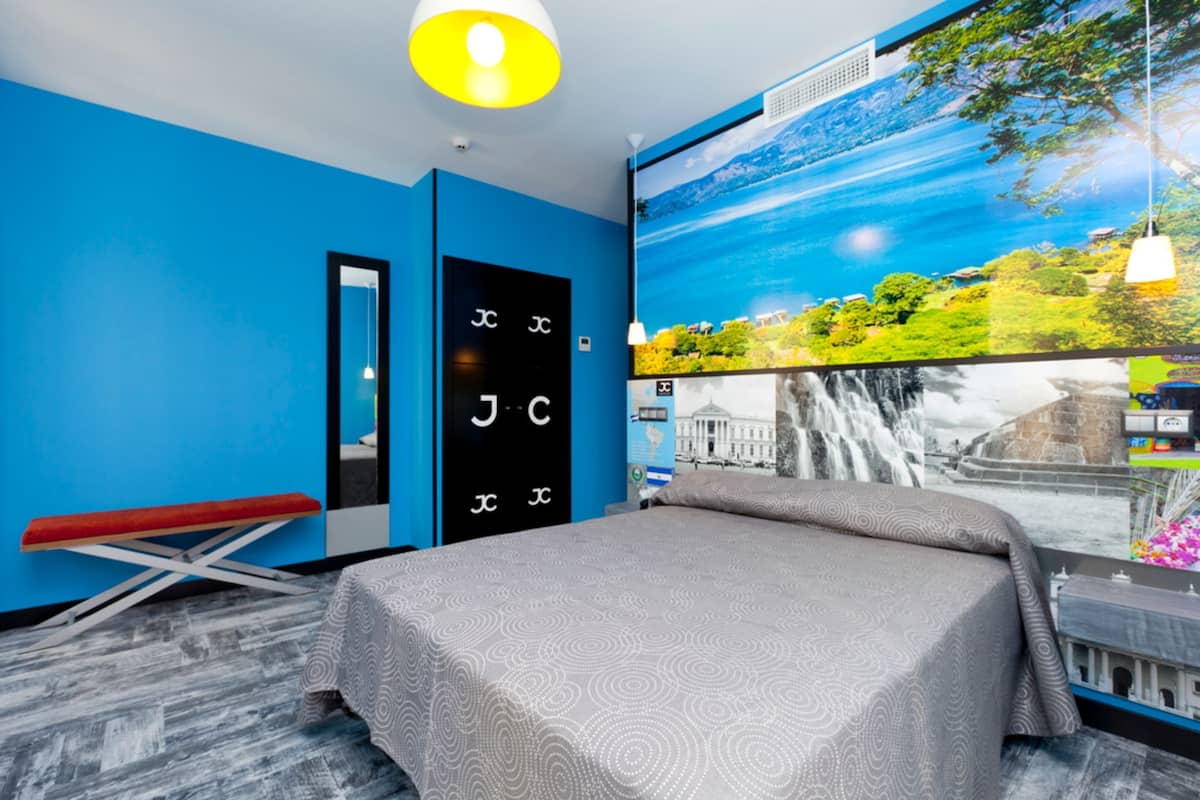 A modern hotel room with a large bed, a bench, a wardrobe, and a large window with a waterfall view.