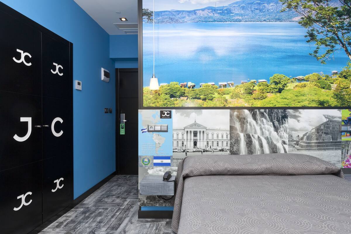 A hotel room with a large window offering a scenic view of a lake and mountains.