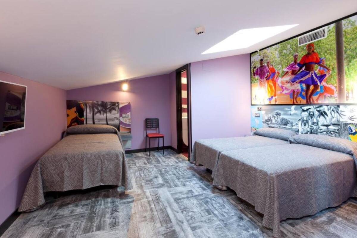 A room with two beds, a chair, and a large window with a view of dancers.