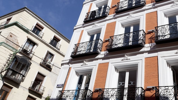 Un edificio de varios pisos con fachadas de ladrillo blanco y rojo, múltiples balcones con barandillas de hierro forjado y un cielo azul despejado al fondo.