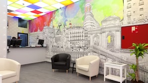 Un área de recepción con un techo colorido, un mural de un paisaje urbano y una puerta roja.