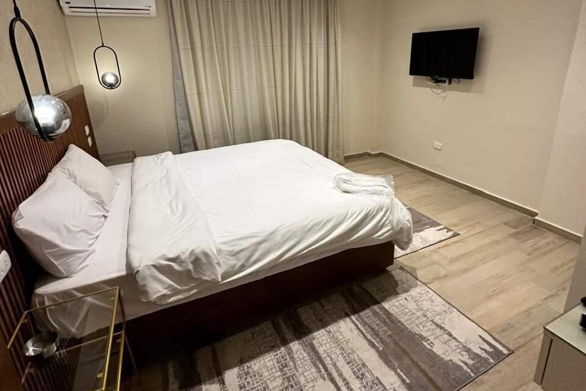 Quarto de hotel moderno com uma cama grande, televisão de tela plana na parede, ar-condicionado no teto e um tapete estampado.