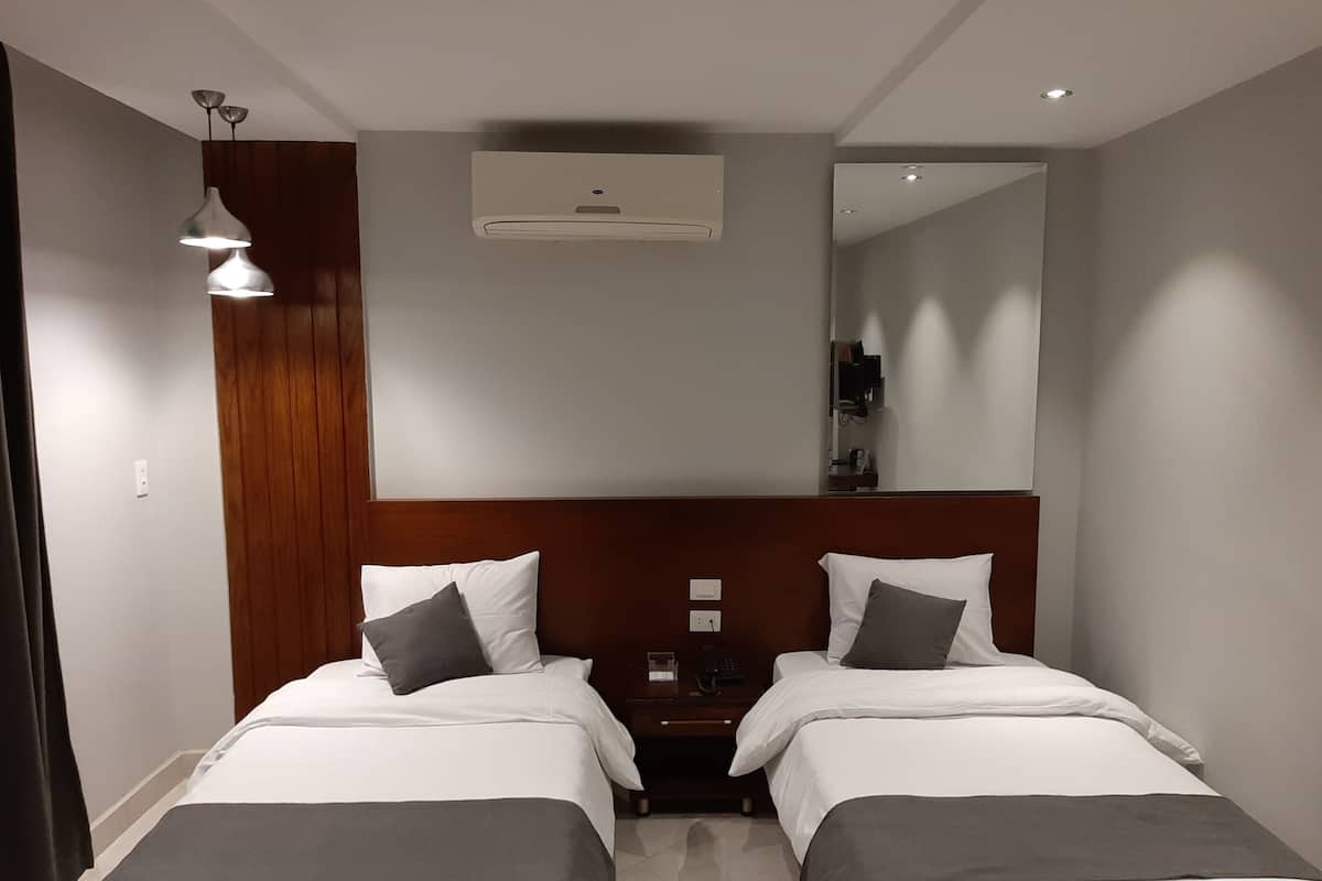 Quarto de hotel com duas camas, cabeceira de madeira, espelho e ar condicionado no teto.