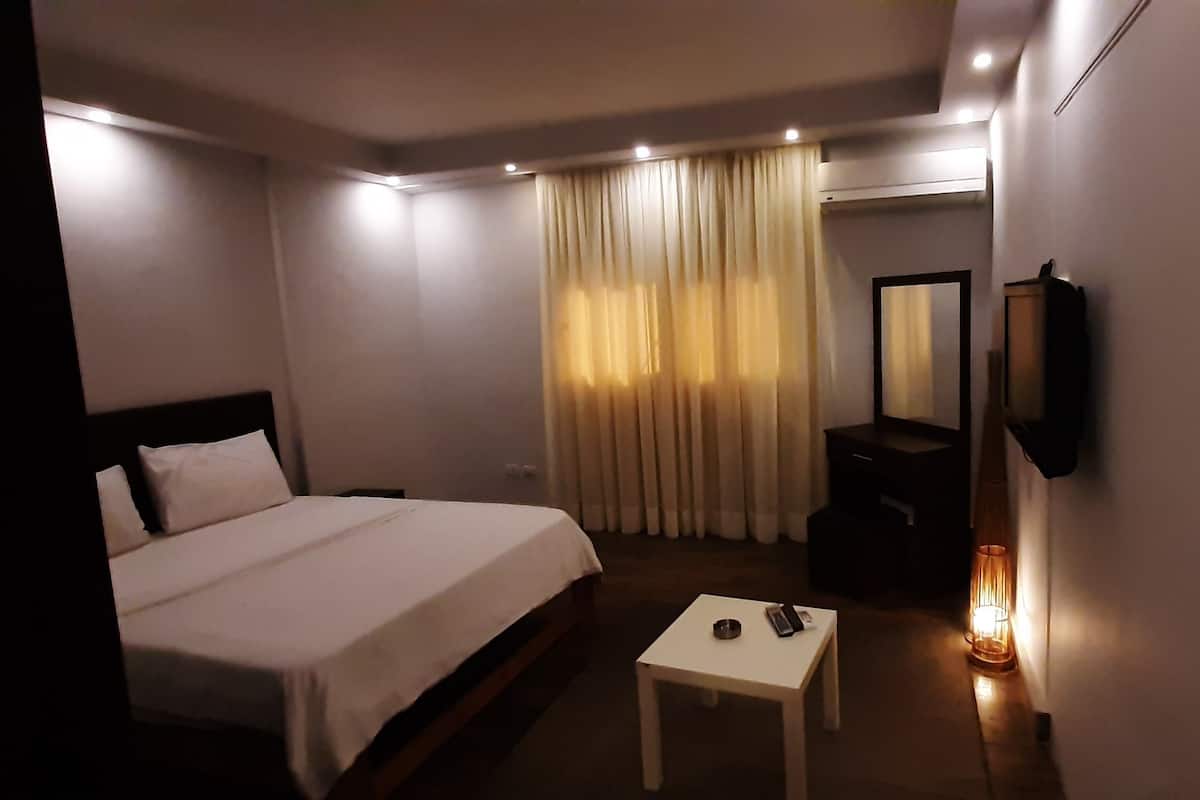 Quarto de hotel com cama, uma mesa pequena, um espelho e televisão presa na parede.
