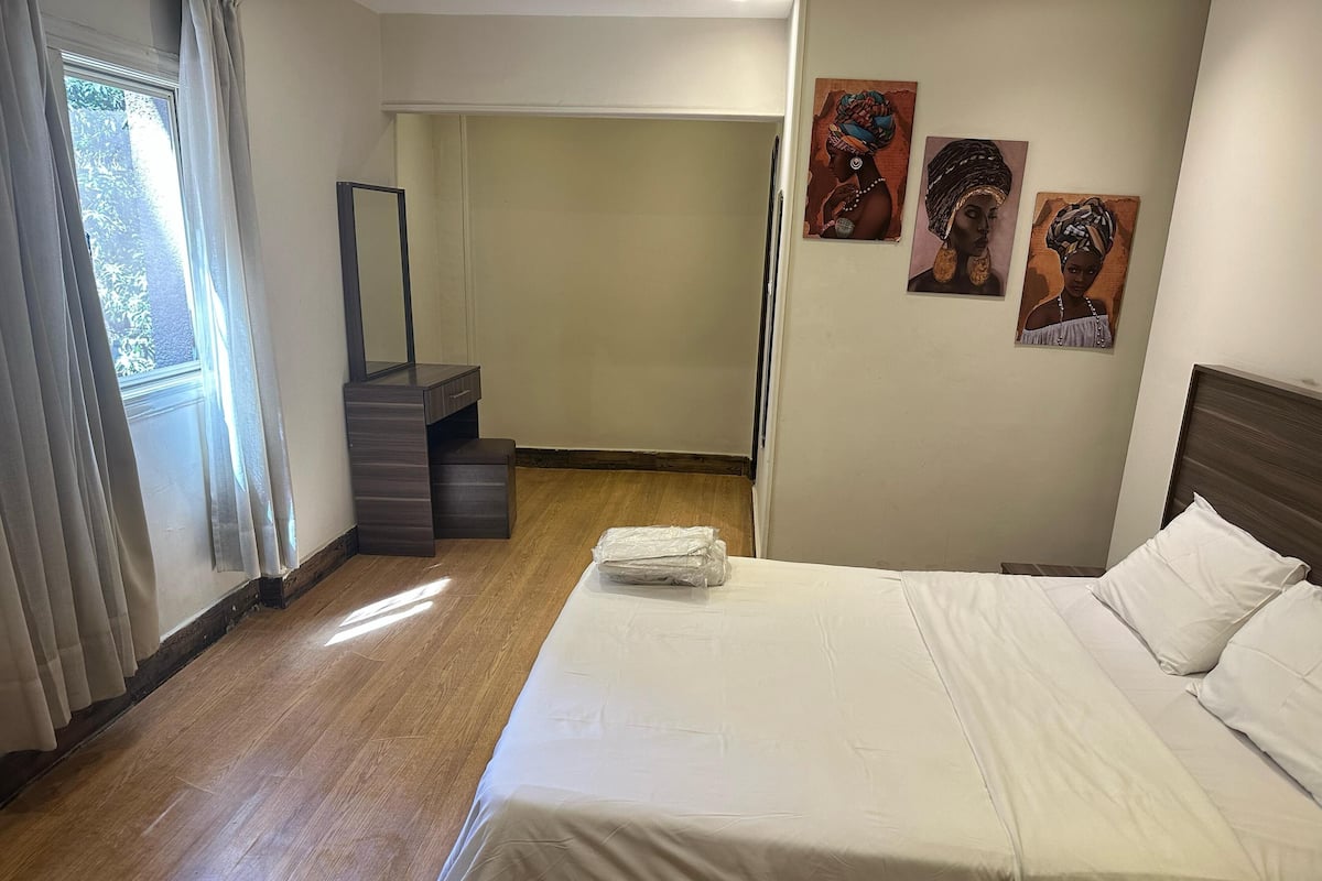 Quarto de hotel com uma cama, uma cômoda, um espelho e três quadros na parede.