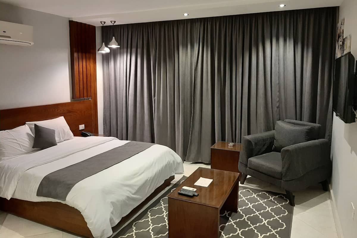 Quarto de hotel com cama, escrivaninha, cadeira, televisão e uma janela grande com cortinas.