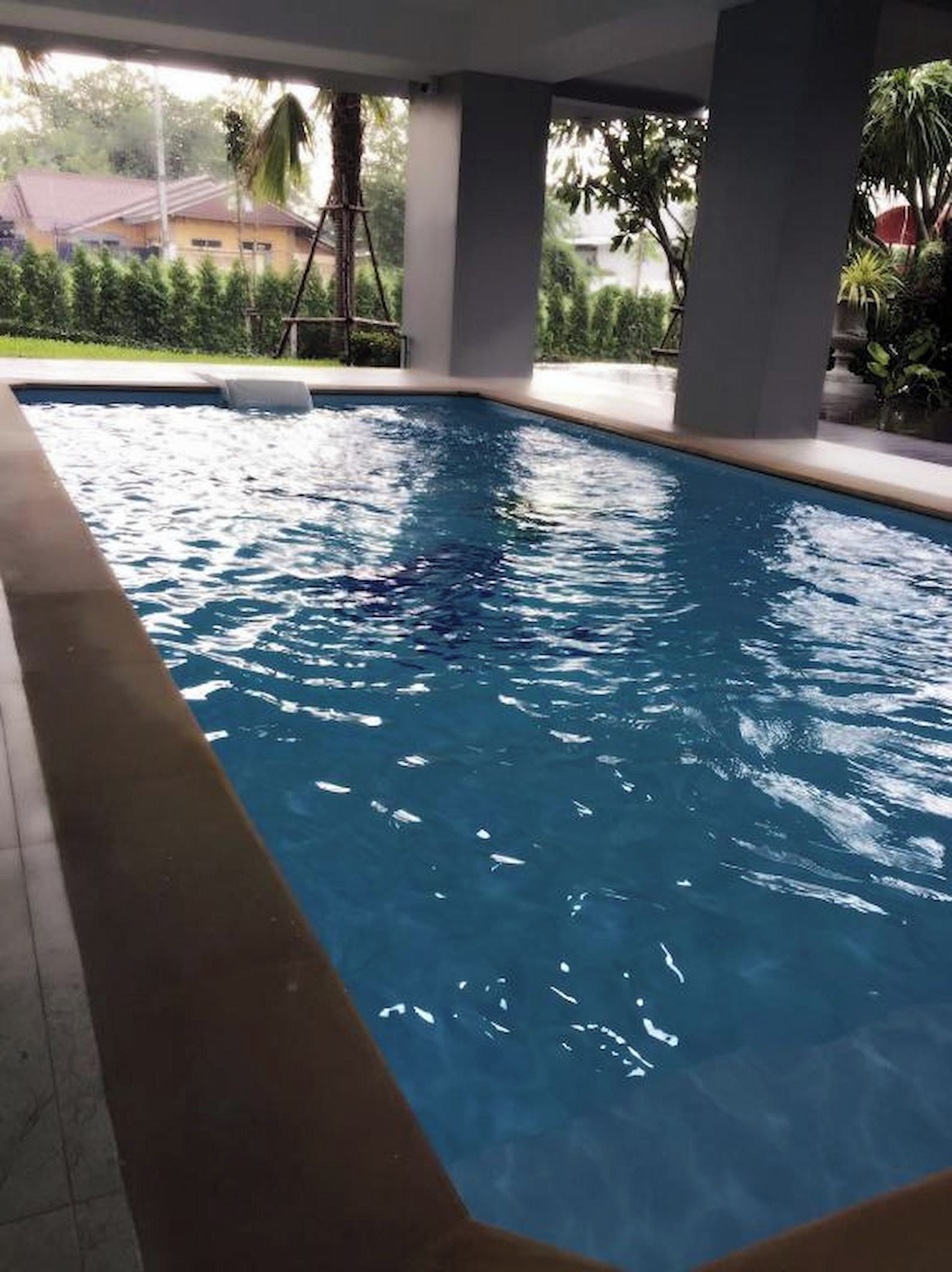 A swimming pool with clear water, surrounded by a tiled deck and concrete pillars.