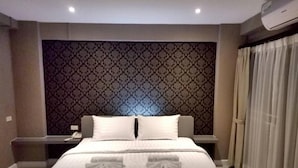 Ein Hotelzimmer mit einem großen Bett, einem gemusterten Kopfteil, einem Nachttisch mit Lampe und einem Fenster mit Vorhängen.