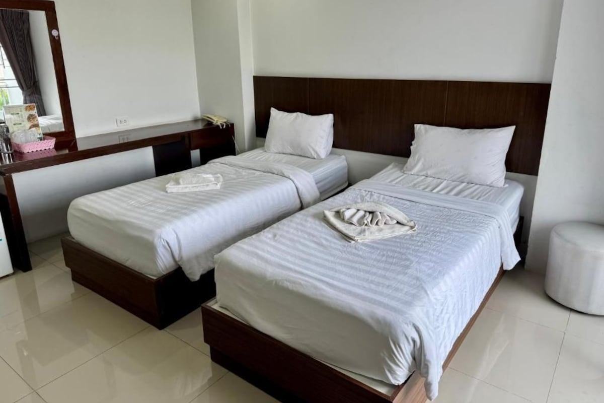 A hotel room with two beds, a wooden headboard, a bedside table, and a mirror.