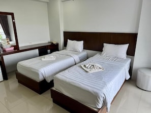 A hotel room with two beds, a wooden headboard, a bedside table, and a mirror. - Nava Grand Hotel (Thanyaburi)