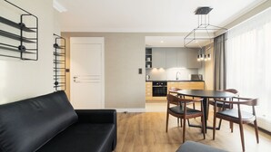 A modern living room with a black sofa, a dining table with four chairs, and a kitchen in the background. - Grand Apartments Victoria Residence (Sopot)