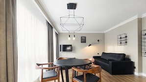 A modern living room with a round wooden table, black chairs, a black sofa, and a geometric ceiling light fixture. - Grand Apartments Victoria Residence (Sopot)