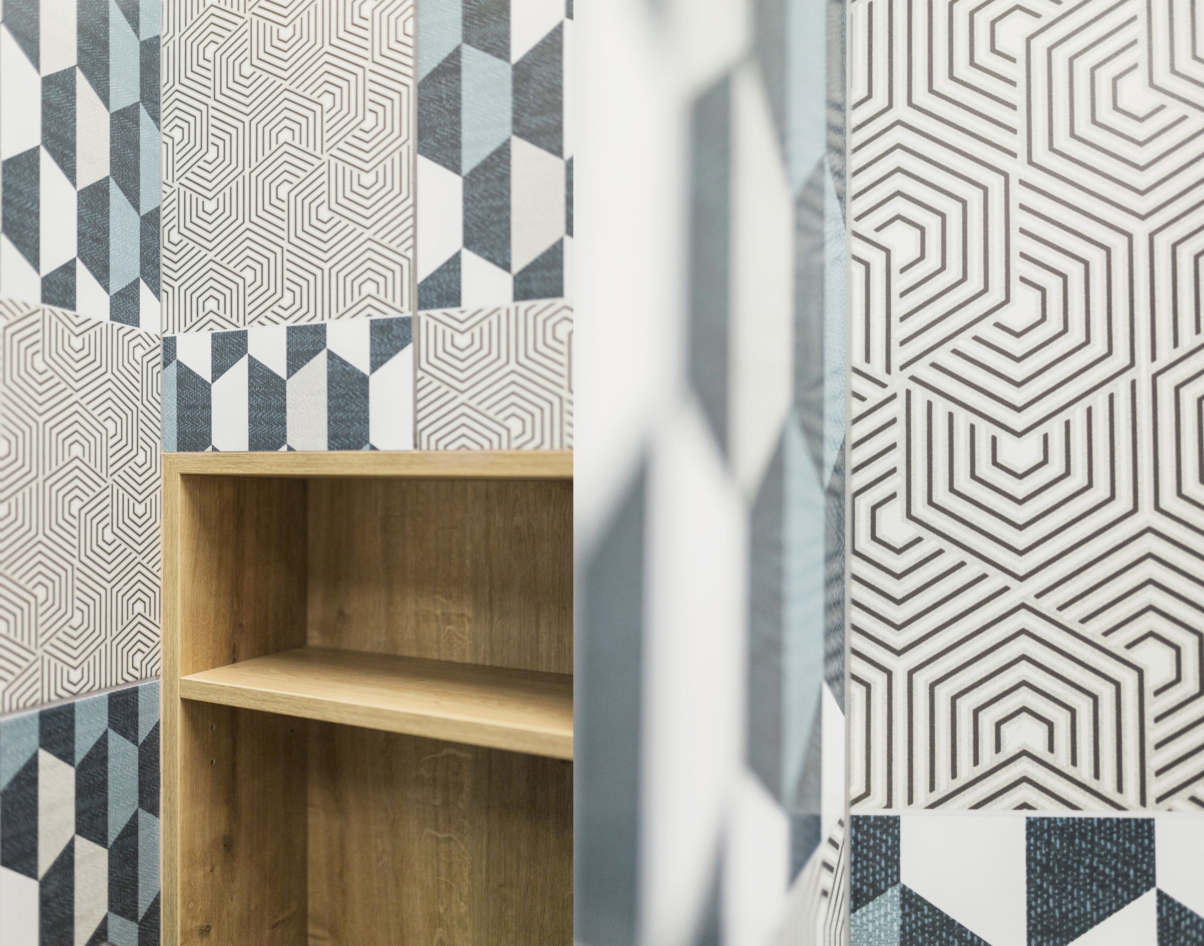 A room with geometric patterned wallpaper, a wooden shelf, and a partially visible curtain.