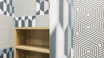 A room with geometric patterned wallpaper, a wooden shelf, and a partially visible curtain.