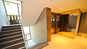 A modern staircase with a glass railing, a concrete wall, and a metal elevator. - Grand Apartments Victoria Residence (Sopot)