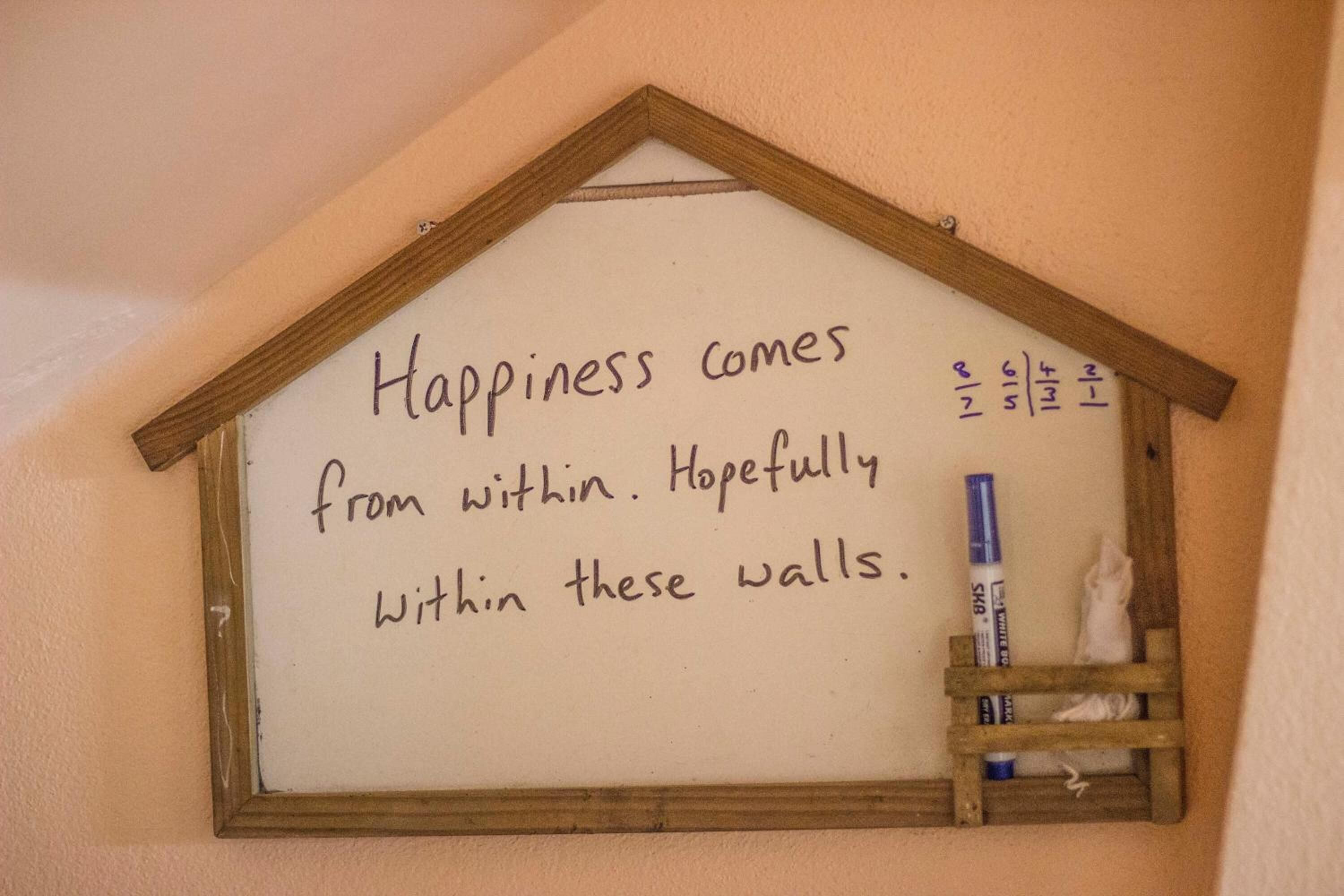 Un letrero escrito a mano en una pared que dice: 'La felicidad viene de dentro. Ojalá dentro de estas paredes'.