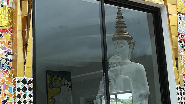 A building facade with colorful mosaic tiles and a large glass window reflecting a Buddha statue. - Karma Home Hostel (Phitsanulok)